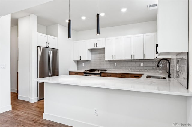 kitchen with sink, stainless steel appliances, kitchen peninsula, pendant lighting, and white cabinets