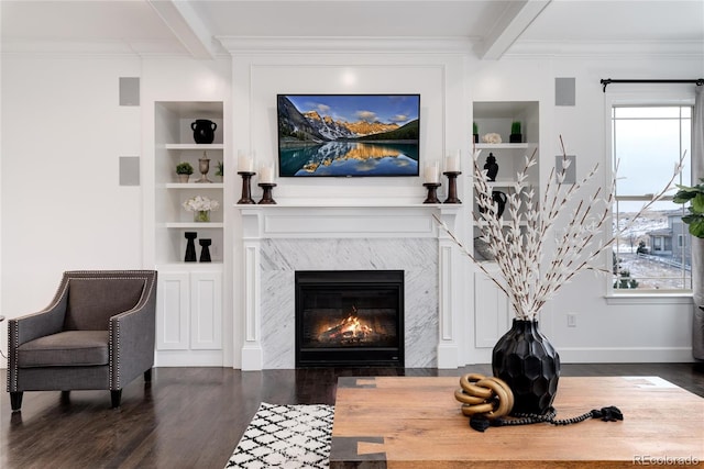 living room with beam ceiling, built in shelves, a premium fireplace, dark hardwood / wood-style flooring, and crown molding