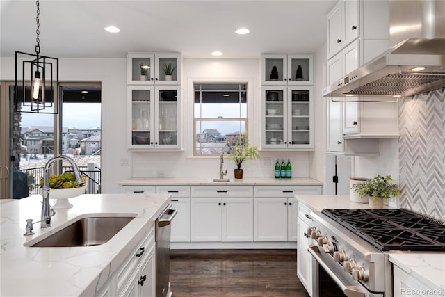 kitchen with light stone counters, wall chimney exhaust hood, stainless steel appliances, sink, and hanging light fixtures