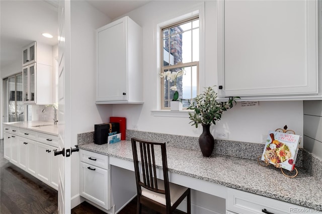 kitchen featuring light stone countertops, built in desk, white cabinetry, and sink