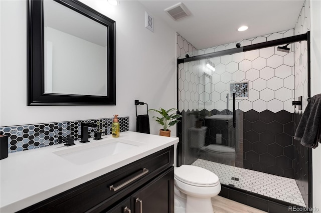 bathroom with vanity, toilet, a shower with door, and tasteful backsplash