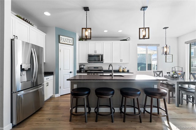 kitchen with sink, white cabinetry, hanging light fixtures, appliances with stainless steel finishes, and an island with sink