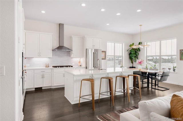 kitchen with backsplash, wall chimney range hood, a breakfast bar, light countertops, and high quality fridge