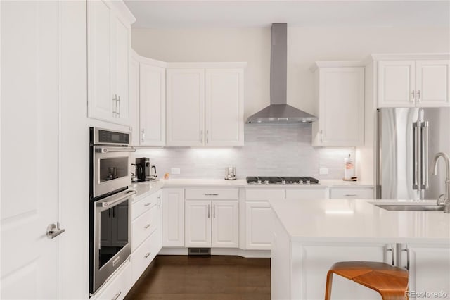 kitchen featuring backsplash, appliances with stainless steel finishes, wall chimney range hood, and a sink