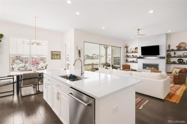 kitchen featuring an island with sink, a sink, stainless steel dishwasher, dark wood finished floors, and a large fireplace