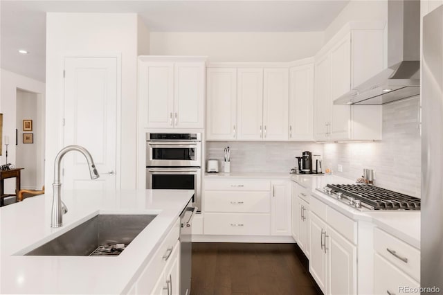 kitchen with a sink, backsplash, stainless steel appliances, white cabinets, and wall chimney range hood