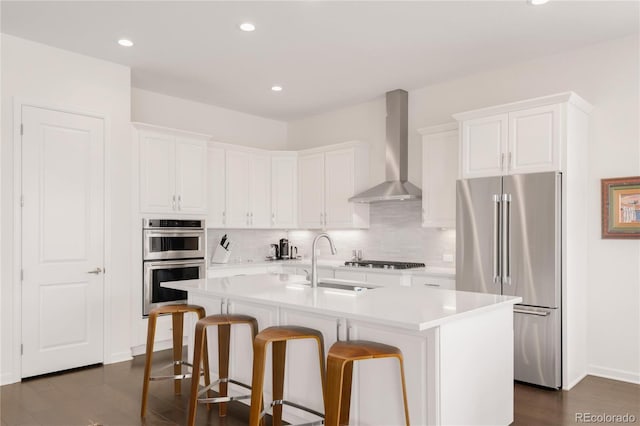 kitchen featuring a sink, appliances with stainless steel finishes, white cabinets, and wall chimney range hood