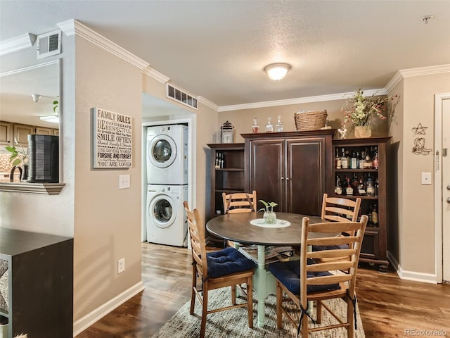 dining room featuring stacked washer and clothes dryer, a textured ceiling, ornamental molding, and dark hardwood / wood-style flooring