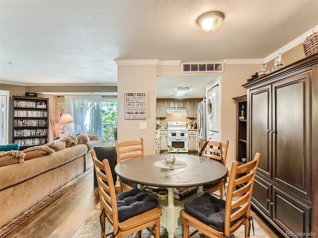 dining room featuring a textured ceiling, crown molding, and light hardwood / wood-style flooring