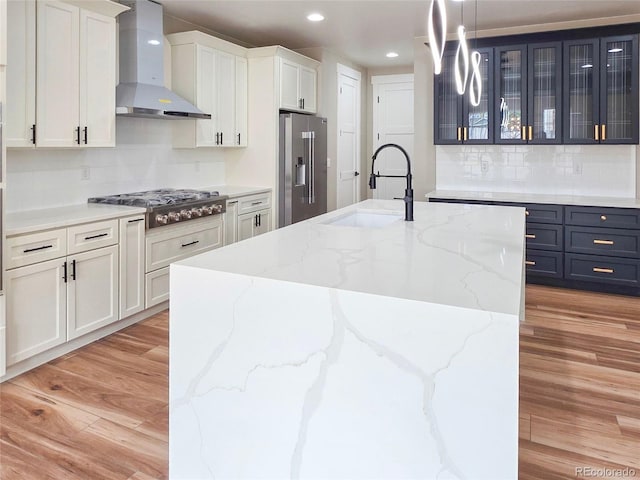 5550 Wetlands Dr, Longmont, CO 80504 - kitchen with wall chimney range hood, appliances with stainless steel finishes, light wood-type flooring, tasteful backsplash, and a kitchen island with sink