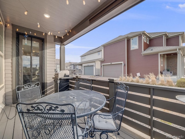deck featuring outdoor dining space, a residential view, grilling area, and an attached garage