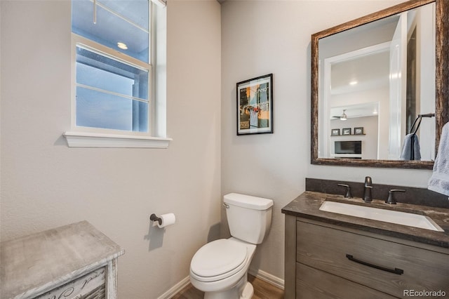 bathroom featuring toilet, ceiling fan, vanity, and baseboards