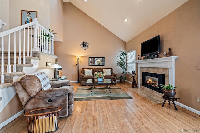 living room featuring a tile fireplace, wood-type flooring, and high vaulted ceiling