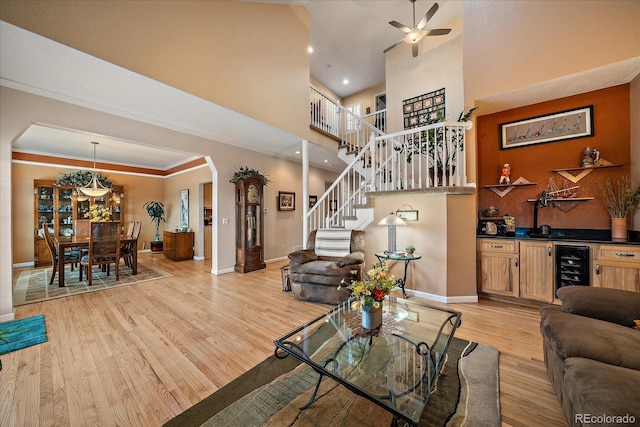 living room with crown molding, a high ceiling, wine cooler, light hardwood / wood-style floors, and indoor bar