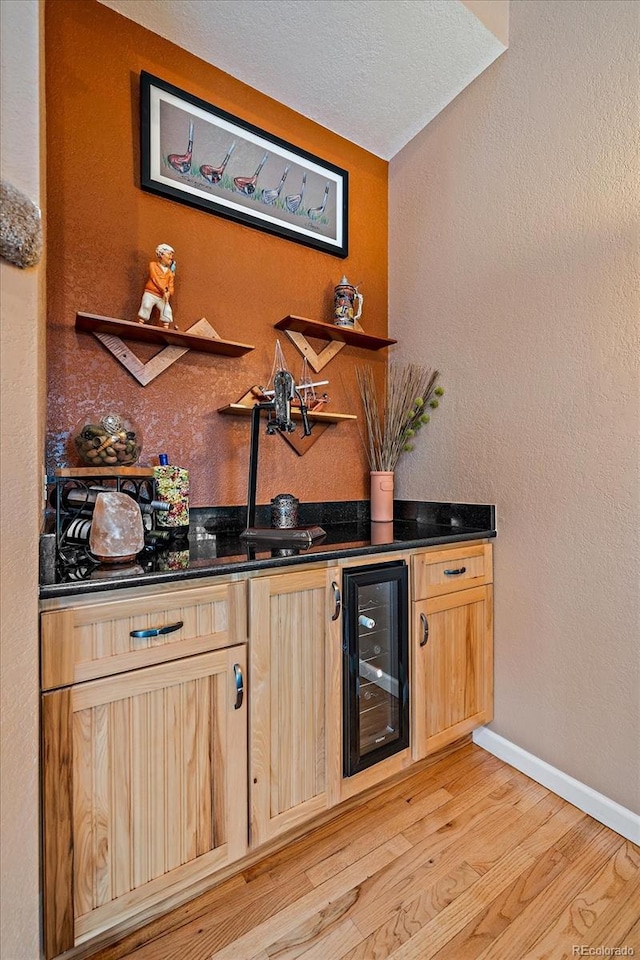 bar featuring a textured ceiling, beverage cooler, light brown cabinetry, and light hardwood / wood-style flooring