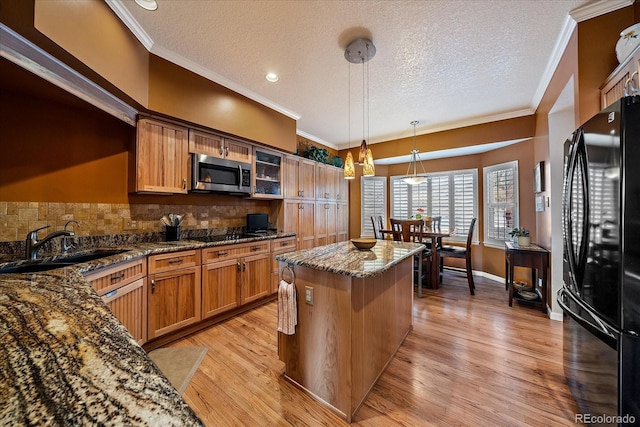 kitchen featuring a kitchen island, sink, dark stone counters, hanging light fixtures, and black appliances