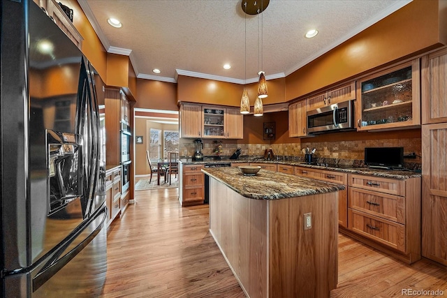 kitchen featuring dark stone countertops, hanging light fixtures, a center island, black appliances, and light hardwood / wood-style flooring