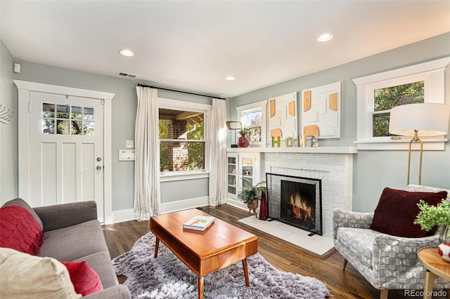 living room with a brick fireplace, plenty of natural light, and dark hardwood / wood-style floors