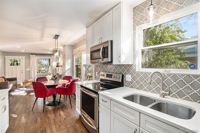 kitchen with appliances with stainless steel finishes, white cabinets, decorative light fixtures, sink, and backsplash