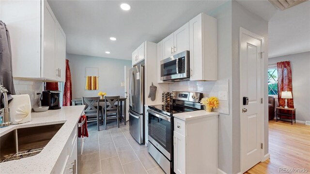 7609 Sherman Pl, Denver, CO 80221 - kitchen featuring sink, stainless steel appliances, light stone countertops, decorative backsplash, and white cabinets
