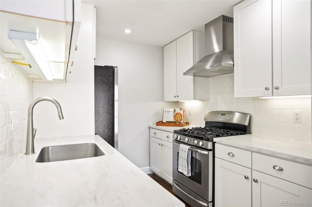 kitchen with stainless steel gas range oven, wall chimney exhaust hood, white cabinets, fridge, and a sink