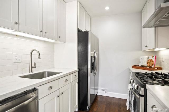 kitchen with dark wood finished floors, a sink, stainless steel appliances, white cabinets, and wall chimney exhaust hood