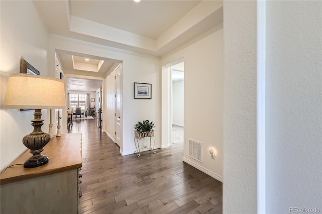 hallway featuring a raised ceiling, wood finished floors, baseboards, and visible vents