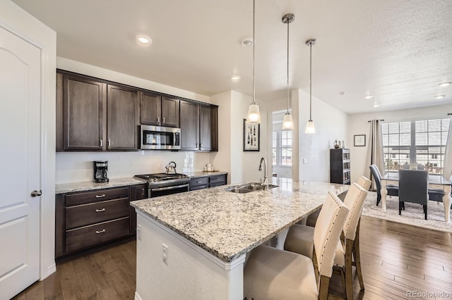 kitchen featuring a sink, dark wood-style floors, stainless steel appliances, a kitchen island with sink, and dark brown cabinets