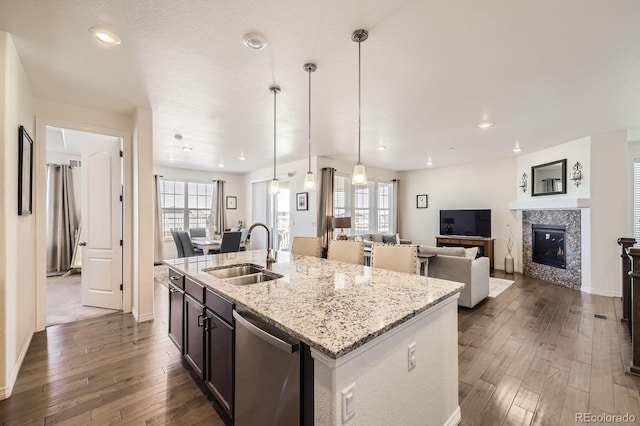 kitchen with open floor plan, dark wood-style flooring, stainless steel dishwasher, a center island with sink, and a sink