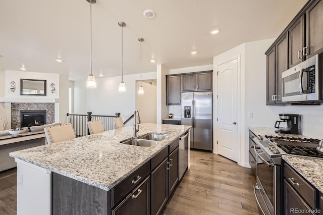 kitchen with light wood-type flooring, a sink, a kitchen island with sink, dark brown cabinetry, and appliances with stainless steel finishes