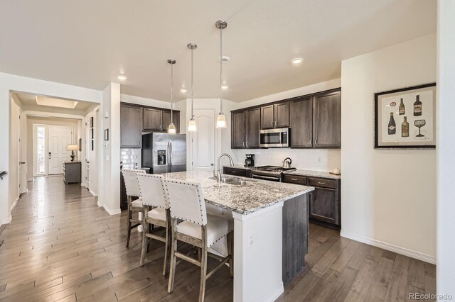 kitchen with a kitchen bar, wood finished floors, dark brown cabinets, appliances with stainless steel finishes, and a sink