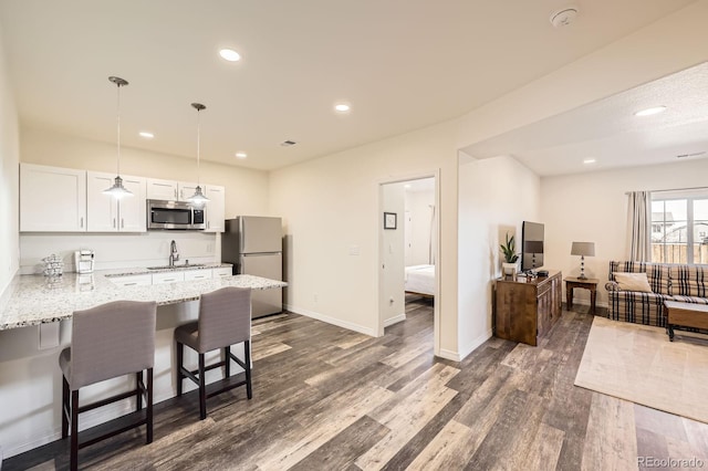 kitchen with stainless steel microwave, a sink, a breakfast bar area, dark wood-style floors, and freestanding refrigerator