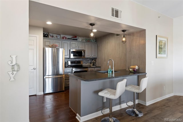 kitchen with kitchen peninsula, pendant lighting, dark hardwood / wood-style floors, appliances with stainless steel finishes, and sink