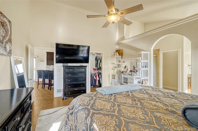 bedroom with a spacious closet, a closet, wood finished floors, arched walkways, and high vaulted ceiling