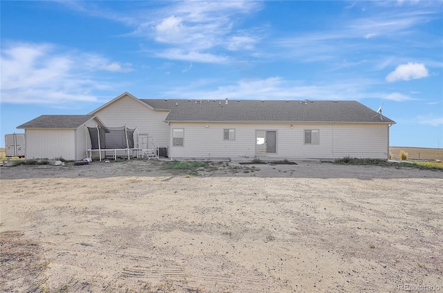 back of house featuring an outdoor structure, a storage unit, and a trampoline