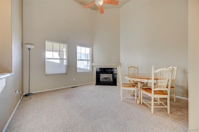 carpeted dining area featuring a tiled fireplace, a towering ceiling, and ceiling fan