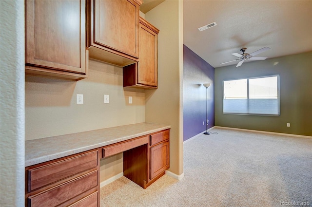 kitchen featuring built in desk, light colored carpet, and ceiling fan