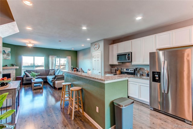 kitchen with a kitchen island, a breakfast bar, white cabinetry, stainless steel appliances, and light stone countertops