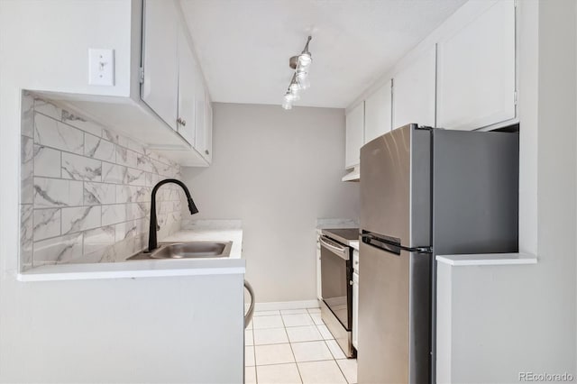 kitchen with stove, sink, light tile patterned floors, white cabinetry, and stainless steel refrigerator