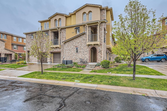 view of front of home with stone siding, a garage, stucco siding, driveway, and a balcony