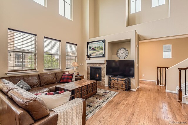 living area with a towering ceiling, a fireplace, stairway, light wood finished floors, and baseboards
