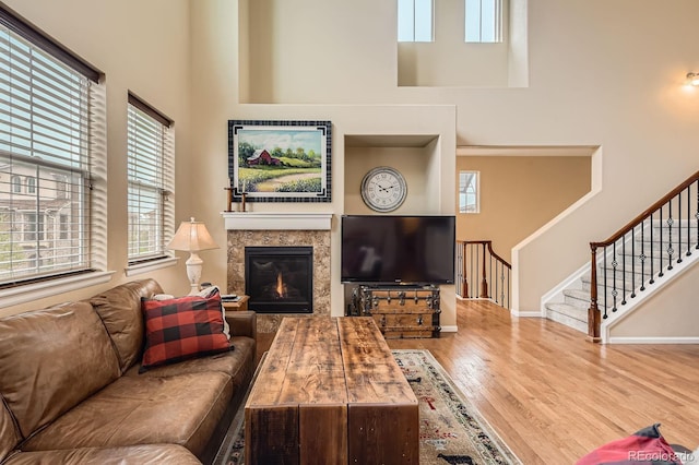 living area featuring wood finished floors, a towering ceiling, baseboards, stairway, and a glass covered fireplace