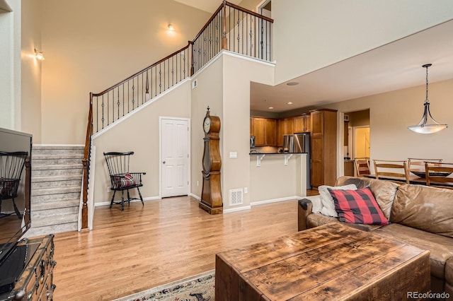 living room with light wood-type flooring, stairway, baseboards, and a high ceiling
