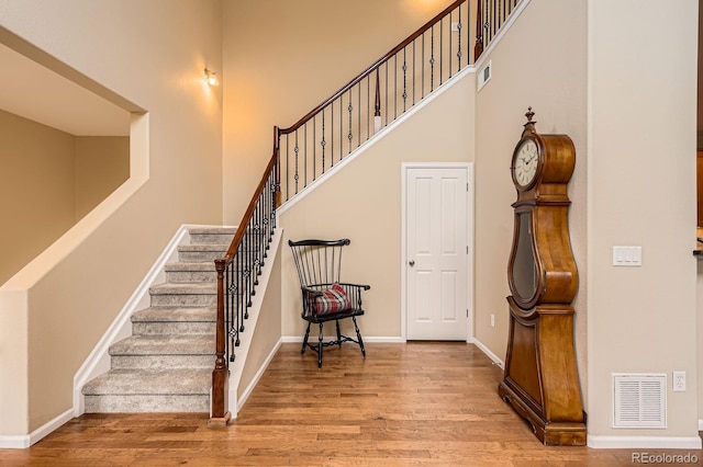 staircase featuring a towering ceiling, wood finished floors, and baseboards
