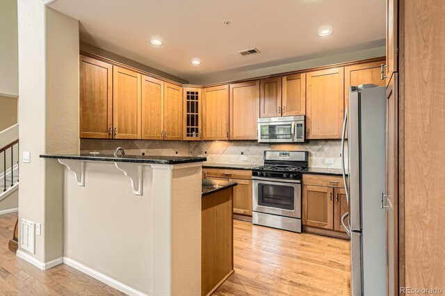 kitchen with stainless steel appliances, a kitchen breakfast bar, a peninsula, light wood-type flooring, and glass insert cabinets