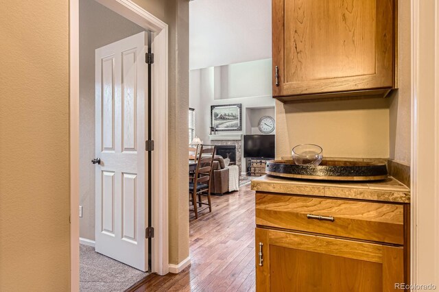 kitchen featuring hardwood / wood-style flooring, a textured wall, a glass covered fireplace, brown cabinets, and baseboards
