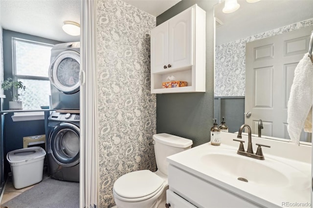 bathroom featuring toilet, stacked washer and clothes dryer, tile patterned flooring, a textured ceiling, and vanity