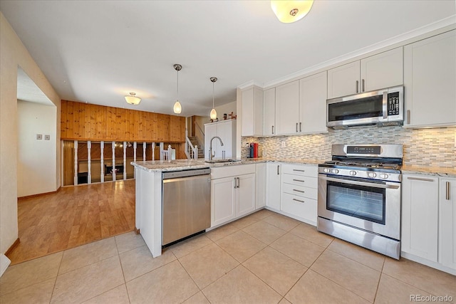 kitchen with stainless steel appliances, a sink, backsplash, a peninsula, and wood walls