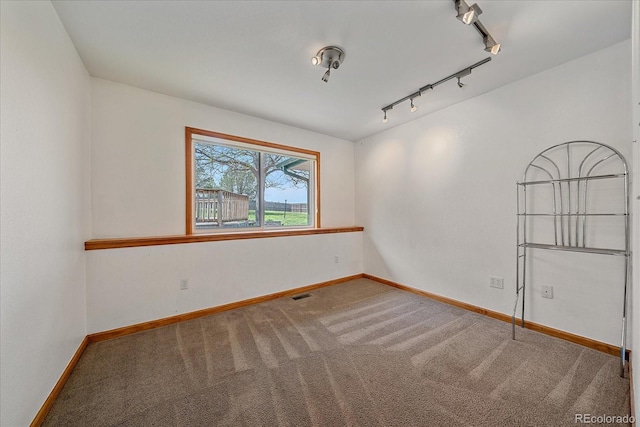spare room featuring carpet flooring, track lighting, and baseboards