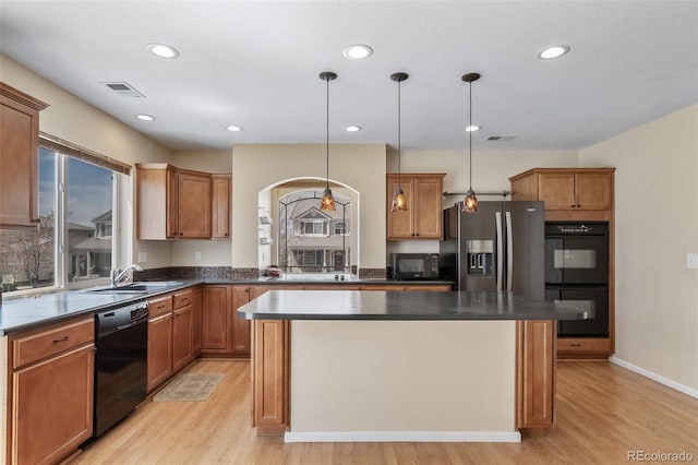 kitchen featuring black appliances, a sink, light wood finished floors, dark countertops, and a kitchen island